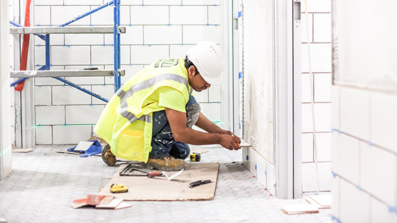 worker installing ceramic tile on wall